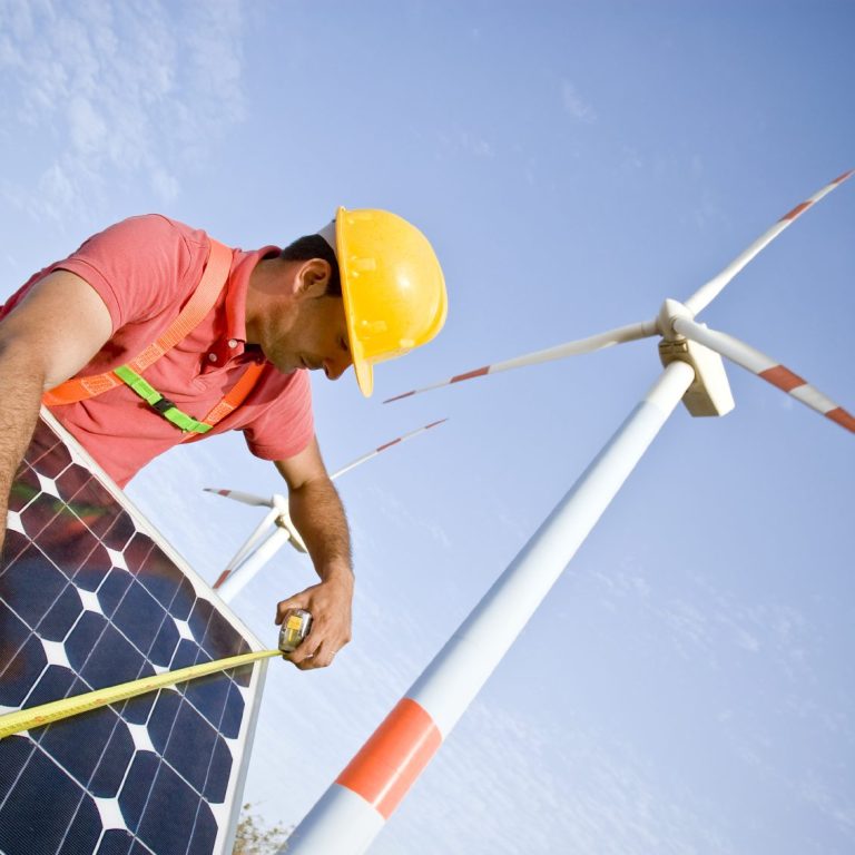 Lavoratore misura un pannello solare vicino a una turbina eolica.